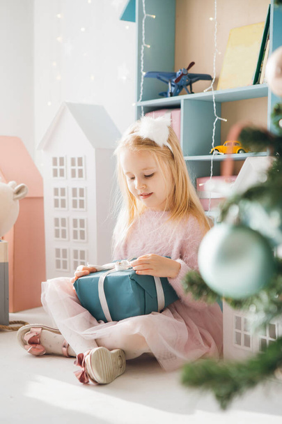 Pretty girl is sitting at the Christmas tree and holding a box with a gift. The holiday concept. Toning. - Valokuva, kuva