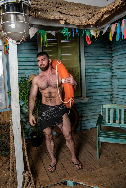 bell'uomo fisicamente ben sviluppato sotto il portico di una casa di pesca vicino al mare - Foto, immagini