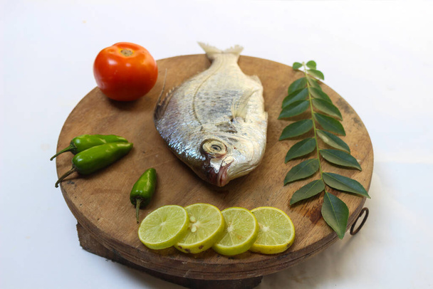 Gerres Fish (Gerres Filamentos)/ウィッフィン・シルバー・ビディー・フィッシュ木のパッドにカレーの葉とトマトで飾られた、白い背景. - 写真・画像