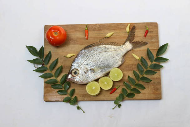 Gerres Fish (Gerres Filamentosus) / Whipfin silver biddy Fish, ozdobiona liśćmi curry i pomidorami na drewnianej podkładce, białe tło. - Zdjęcie, obraz