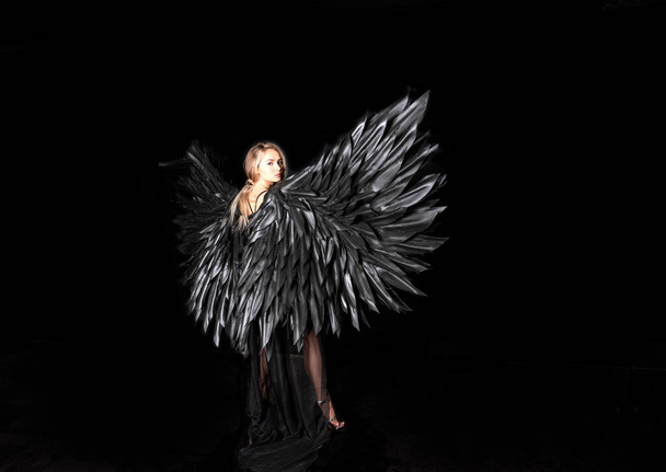 όμορφη ξανθιά κοπέλα σε μαύρο κοστούμι με μαύρα φτερά σε μαύρο φόντο - Φωτογραφία, εικόνα