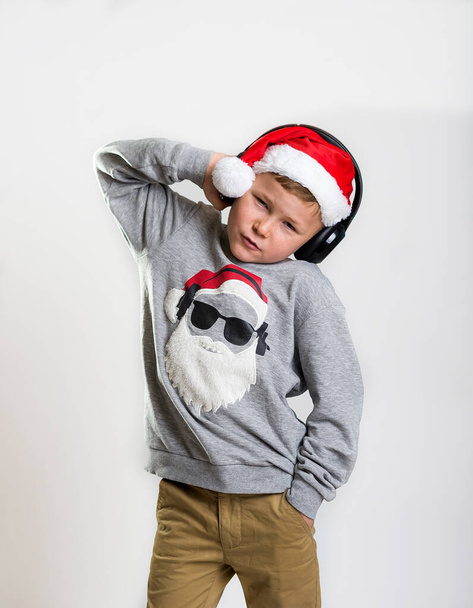 Vacaciones de Navidad. Niño con estilo en auriculares escuchando música en jersey de Navidad. Concepto popular de música y tecnología - Foto, Imagen