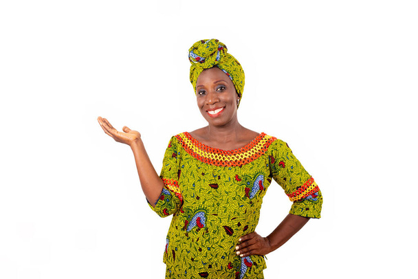 Hermosa mujer adulta africana con un taparrabos y una bufanda verde en la cabeza con el brazo cruzado y la mano levantada sonriendo - Foto, Imagen