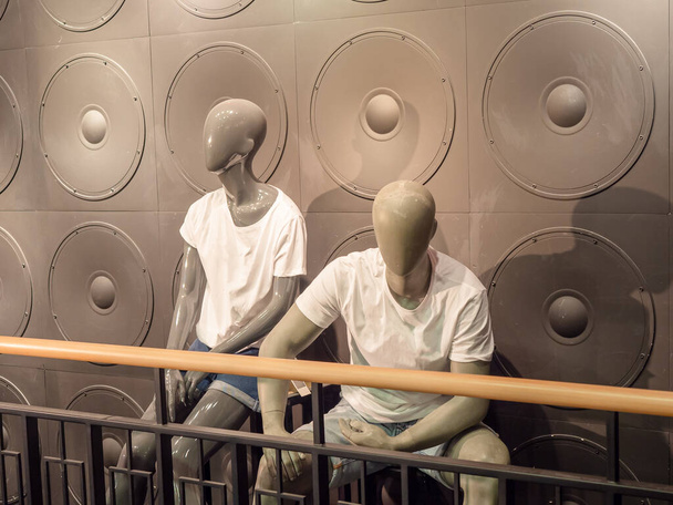 Beyaz tişörtlü erkek ve kadın yüzsüz mankenler gri desenli bir duvara yaslanır. - Fotoğraf, Görsel