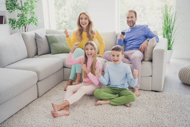 Full size photo of crazy family people mommy daddy two small kids watch sport film movie raise fists sit sofa floor in house indoors - Valokuva, kuva