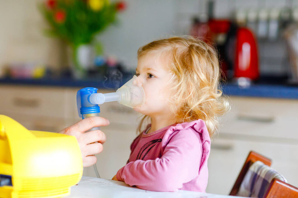 Little toddler girl making inhalation with nebulizer at home. Father or mother helping and holding the device. Child having flu, cough and bronchitis. asthma inhaler inhalation steam sick concept - Photo, Image