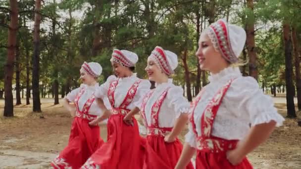 Vista lateral de cuatro mujeres jóvenes bailando Danzas tradicionales rusas en el bosque de verano - Imágenes, Vídeo