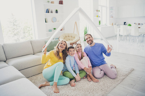 Full body photo of harmony family people mommy daddy sit floor hold paper card roof above two little kids in house indoors - Foto, afbeelding