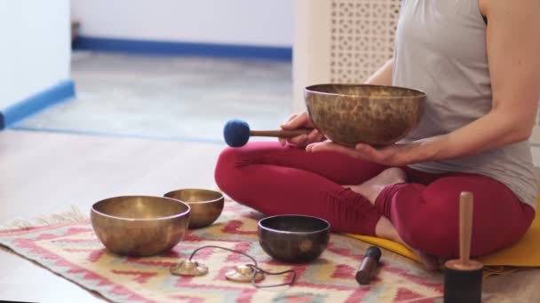 Donna che gioca sulla ciotola tibetana mentre siede sul tappetino yoga. Annata tonica. filmati di magazzino. Video del rallentatore. Da vicino. - Filmati, video