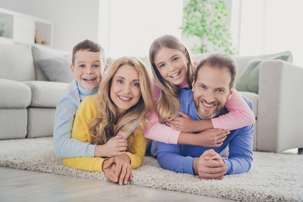 Photo of positive cheerful mommy daddy lying carpet hug two kids boy girl piggyback in house indoors - Photo, Image
