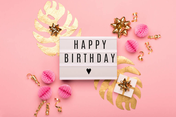 White lightbox with text Happy Birthday, festive gift box, golden and pink decorations on pink paper background. Holiday birthday card concept. Flat lay, top view, copy space. - Foto, afbeelding