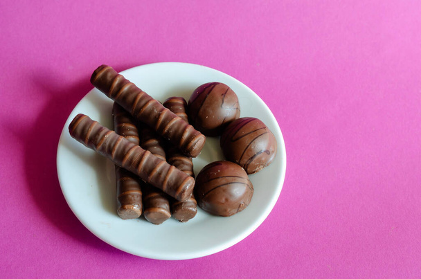 Random Chocolates in white saucer on pink background. Portion of assorted Confectionery. Sweet treats. Selective focus. - Photo, Image