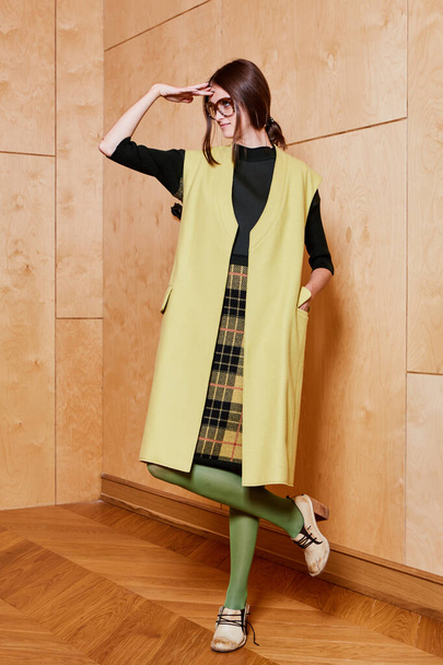 Full length portrait of a pretty brunette girl wearing a black shirt and plaid skirt and in green tights. Standing pose on plywood background. - 写真・画像