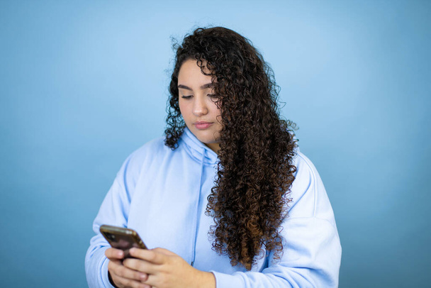 Young beautiful woman wearing casual sweatshirt over isolated blue background texting with her phone - Photo, Image
