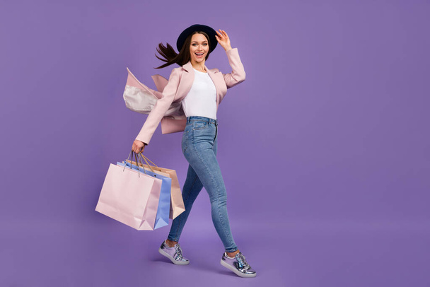 Full length photo positive girl shopping center client hold many bags her hair fly air wind she touch hand headwear wear beige spring outfit denim jeans shoes isolated violet color background - Photo, image