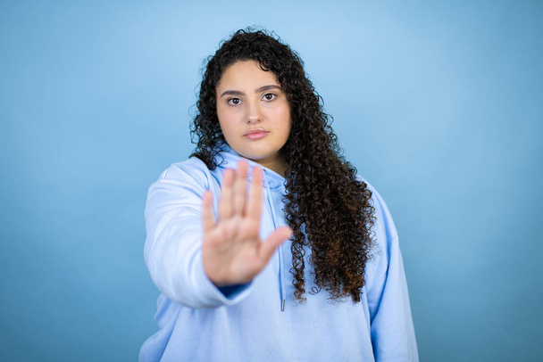 Junge schöne Frau trägt lässiges Sweatshirt über isoliertem blauem Hintergrund ernst und tut Stopp-Singen mit der Handfläche. - Foto, Bild