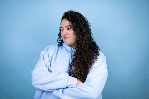 Молода красива жінка в повсякденному светрі над ізольованим синім тлом думає, що виглядає втомленою і нудною з схрещеними руками
 - Фото, зображення
