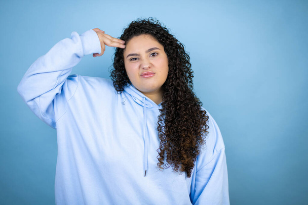 Young beautiful woman wearing casual sweatshirt over isolated blue background Shooting and killing oneself pointing hand and fingers to head like gun, suicide gesture. - Photo, Image