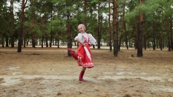 Молодая и красивая женщина в красно-русском традиционном костюме танцует русские танцы в летнем лесу - Кадры, видео