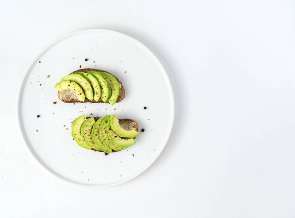 Two avocado and rye bread sandwiches in a white dish on a white background. - Photo, image