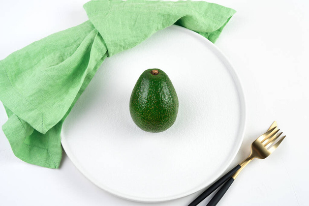 Rijp avocado in een bord naast een groen servet en bestek op een lichte achtergrond. - Foto, afbeelding