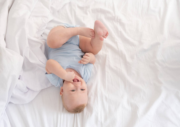 funny baby boy lying on bed at home on white bedding. top view. - Photo, Image