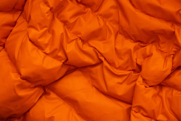 Orange fabric of a warm puffed jacket as a background close up - Фото, изображение