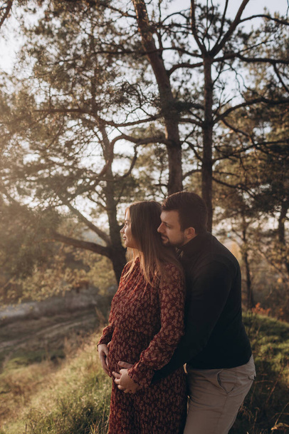 Happy and young pregnant couple hugging in nature - Foto, Bild