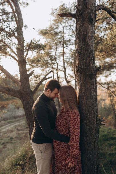 Feliz y joven pareja embarazada abrazándose en la naturaleza - Foto, Imagen