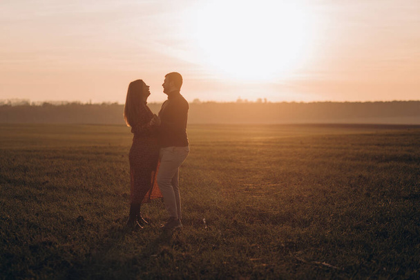 Aviomies ja hänen raskaana oleva vaimonsa kävelevät auringonlaskun aikaan ulkona pellolla. - Valokuva, kuva