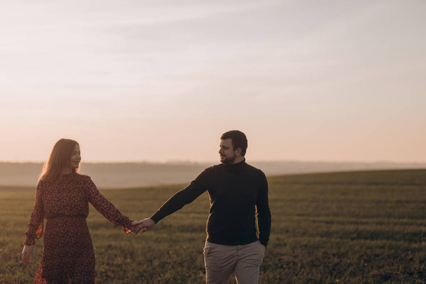 Marito e sua moglie incinta stanno camminando al tramonto sul campo all'esterno - Foto, immagini