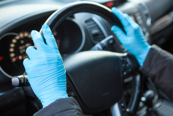 Ihmisen kädet sinisissä lääketieteellisissä käsineissä ohjauspyörää pidellen. Suojaus Covid-19-virukselta, lähikuva - Valokuva, kuva