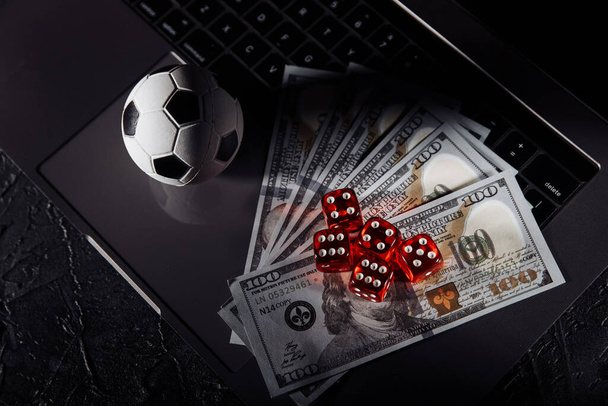 Dice, soccer ball and dollar banknotes on laptops keyboard. Gambling and betting concept - Photo, Image