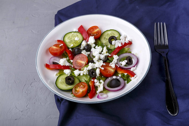 Light plate of Greek salad on a blue napkin on a concrete background. Horizontal photo - Фото, изображение