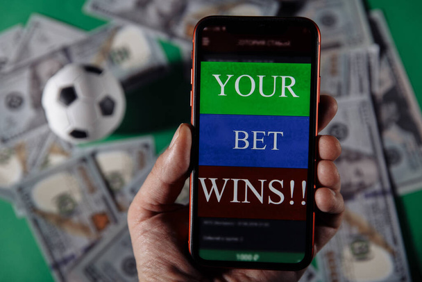 Smartphone with gambling mobile application and soccer ball on green background. Bet wins - Photo, Image