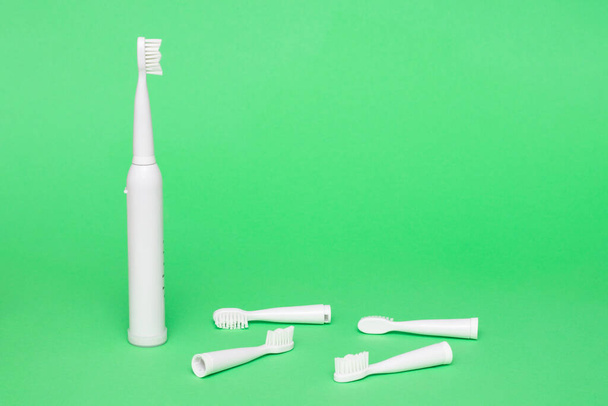 Witte draadloze elektrische tandenborstel met verwisselbare koppen op een lichtgroene achtergrond, kopieerruimte - Foto, afbeelding