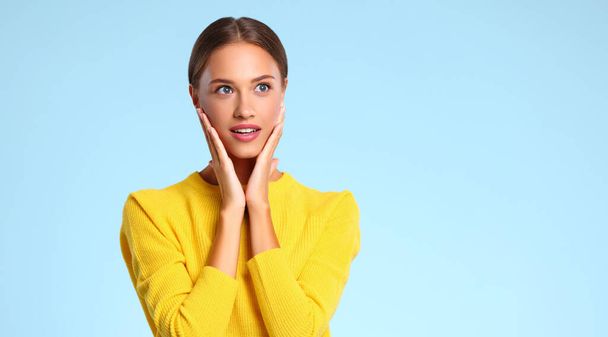 happy emotional surprised woman in a yellow sweater on a blue backgroun - Photo, Image
