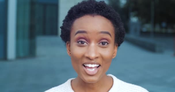 Buiten portret zwarte vrouw Afrikaans meisje vriend buitenlandse student draagt wit zwaaien hallo zegt hi maakt welkome hand gebaar spreekt tot camera spreekt vriendelijk staan op straat in de stad, close-up - Video