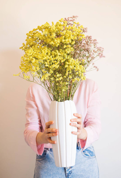 Jonge vrouw in roze shirt met vaas van bloemen - Foto, afbeelding