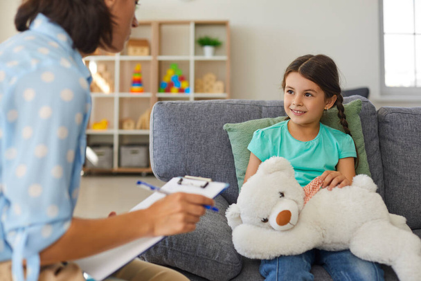 Cute little girl talking to child psychologist during therapy session in cozy modern office - Foto, Bild