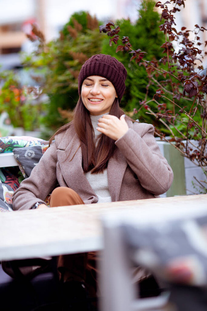 długowłosy brunetka siedzi przy stole w ulicznej kawiarni - Zdjęcie, obraz