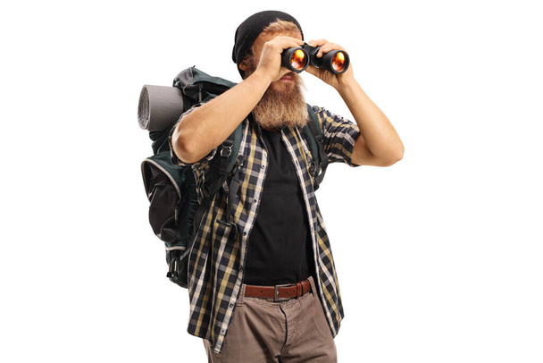 Bearded hiker with a backpack looking through binoculars isolated on white background - Zdjęcie, obraz
