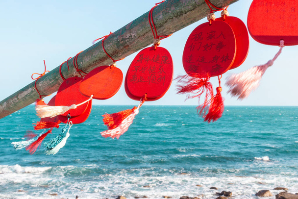 China, isla de Hainan, Sanya - 21 de enero de 2020: Placas rojas chinas con los deseos colgando y balanceándose en el viento en la Zona Cultural Budista de Nanshan. Movimiento borroso de fuertes vientos, enfoque selectivo - Foto, imagen