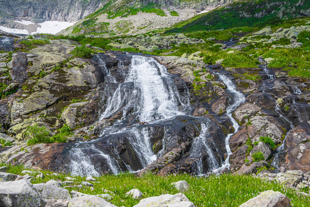 Rapid stream in mountain valley among grassy banks. Small waterfall in green meadow. - Фото, зображення