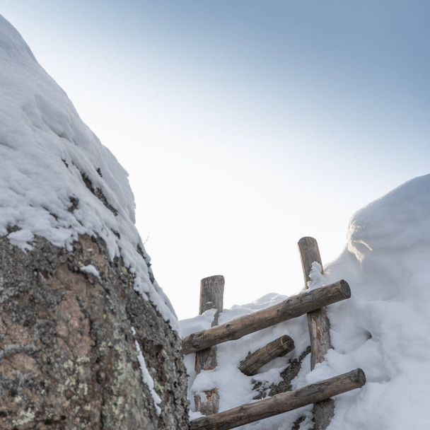 Vieja escalera de madera en la cara cubierta de nieve acantilado. Escalada en roca en invierno - Foto, imagen