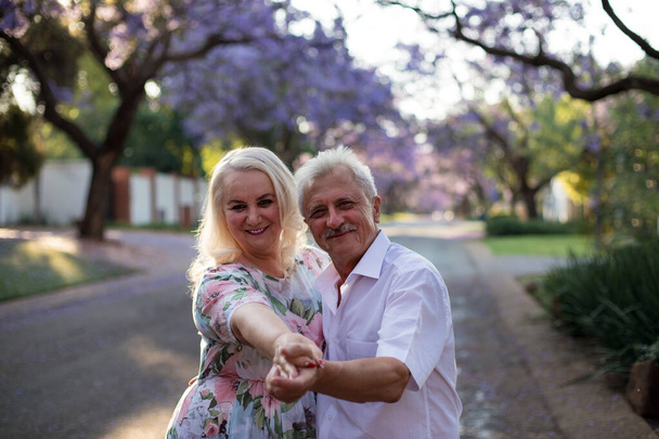 Älteres Paar, Menschen auf der Straße mit blühenden Jacaranda-Bäumen in Pretoria. Ältere Männer und Frauen. Internationaler Tag der älteren Menschen. - Foto, Bild