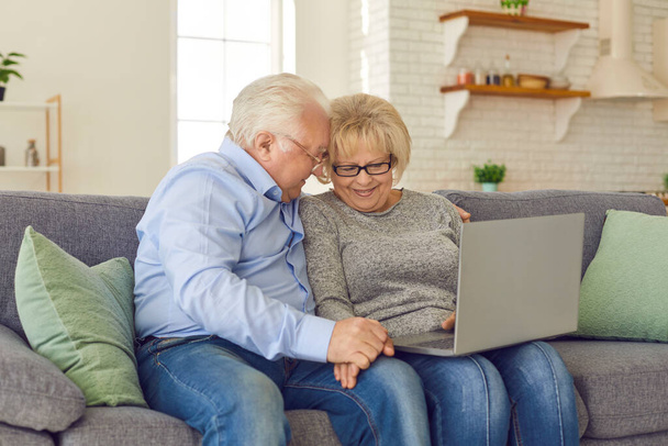 Loving senior couple communicating or ordering something online on laptop at home - Фото, зображення