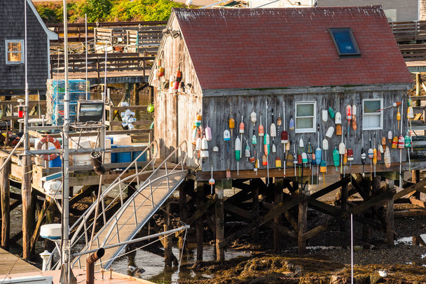 Renkli şamandıraları olan ahşap balıkçı kulübesi gün batımında bir limanın dış duvarında asılı. - Fotoğraf, Görsel