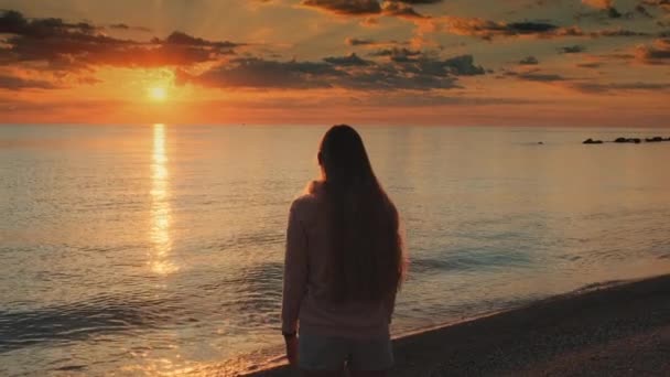 Nainen ojennetuin käsin nauttien auringonlaskun kauneudesta merellä - Materiaali, video