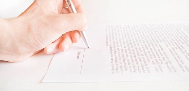 Close-up of the hands of a man wearing white shirt while signing with a pen an official paper document or agreement, placed on a black reflective table, with copy space on black background. - Foto, imagen